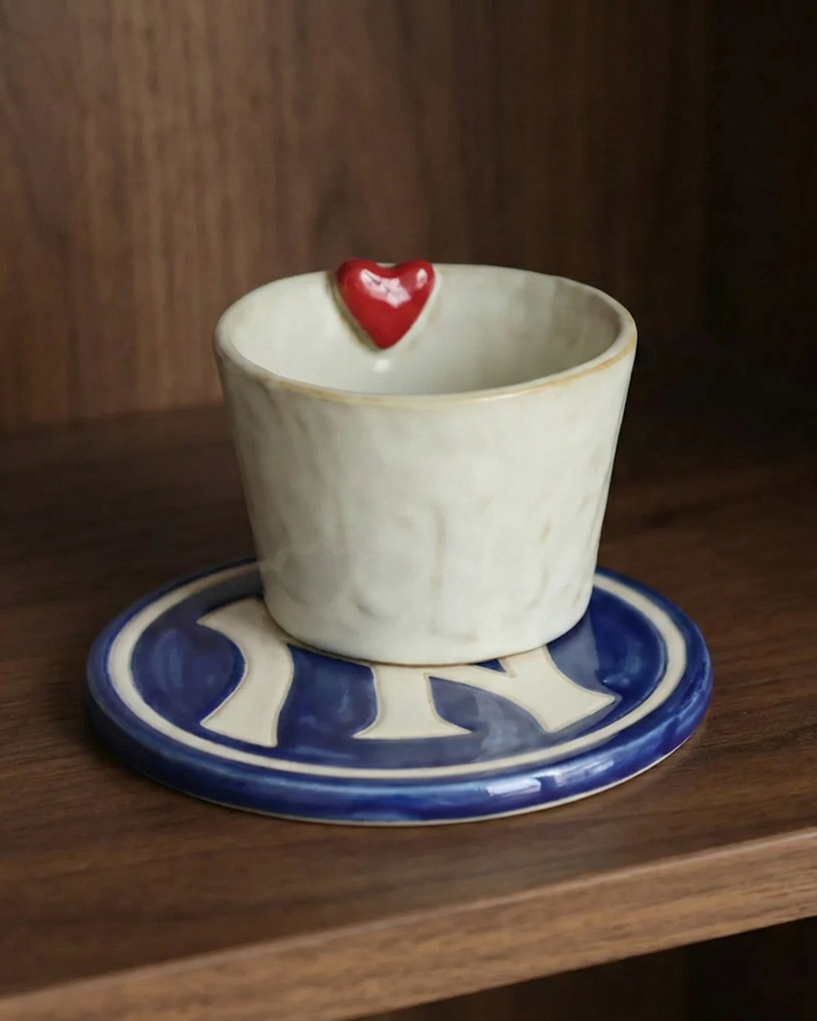 Ceramic cup with a red heart on a matching saucer on a wooden surface