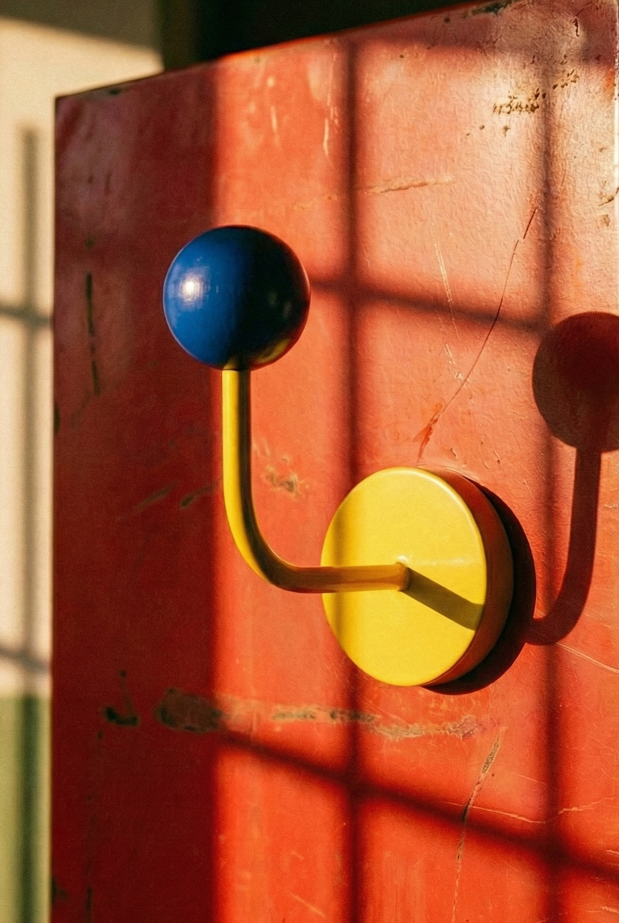 Red wall-mounted cabinet with colorful hooks casting shadows on a wall.