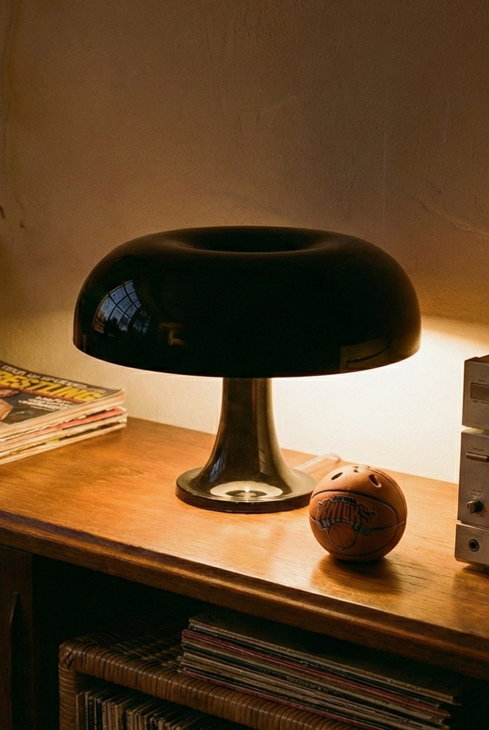 Wooden shelf with a black lamp, magazines, and vintage audio equipment in a dimly lit room.