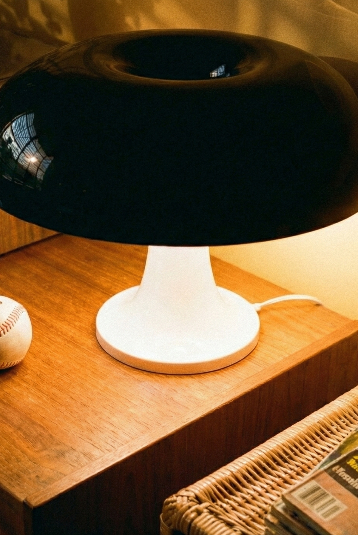 Black and white lamp on a wooden surface with a baseball and magazines in the background