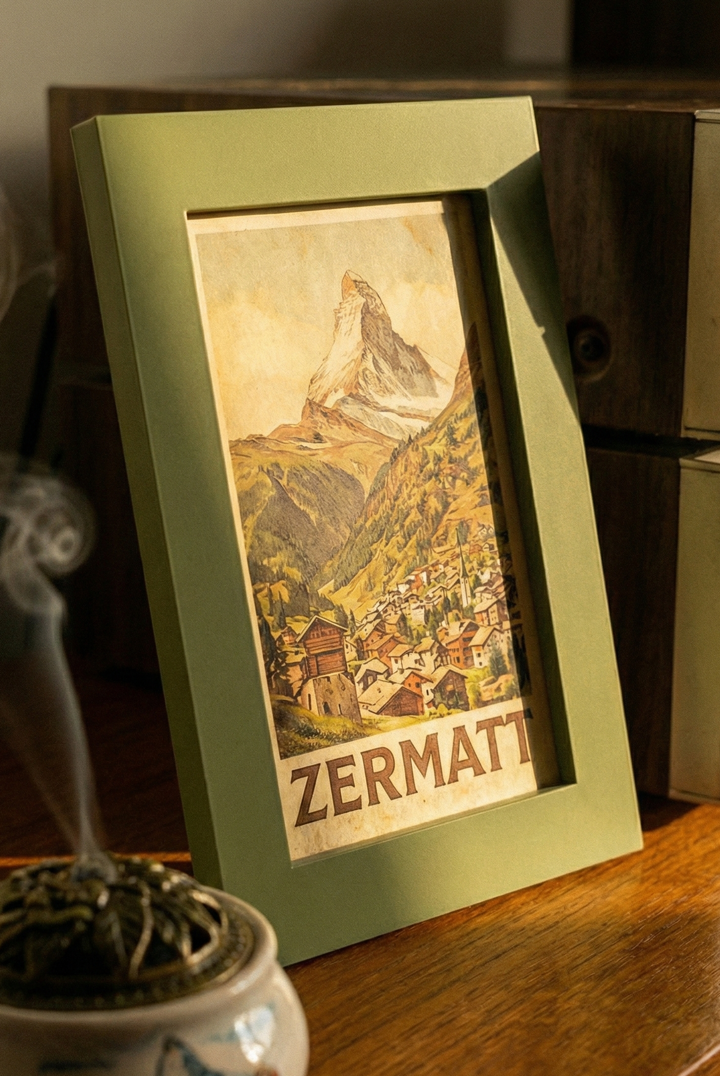 Framed picture of Zermatt with a smoking incense burner on a wooden surface