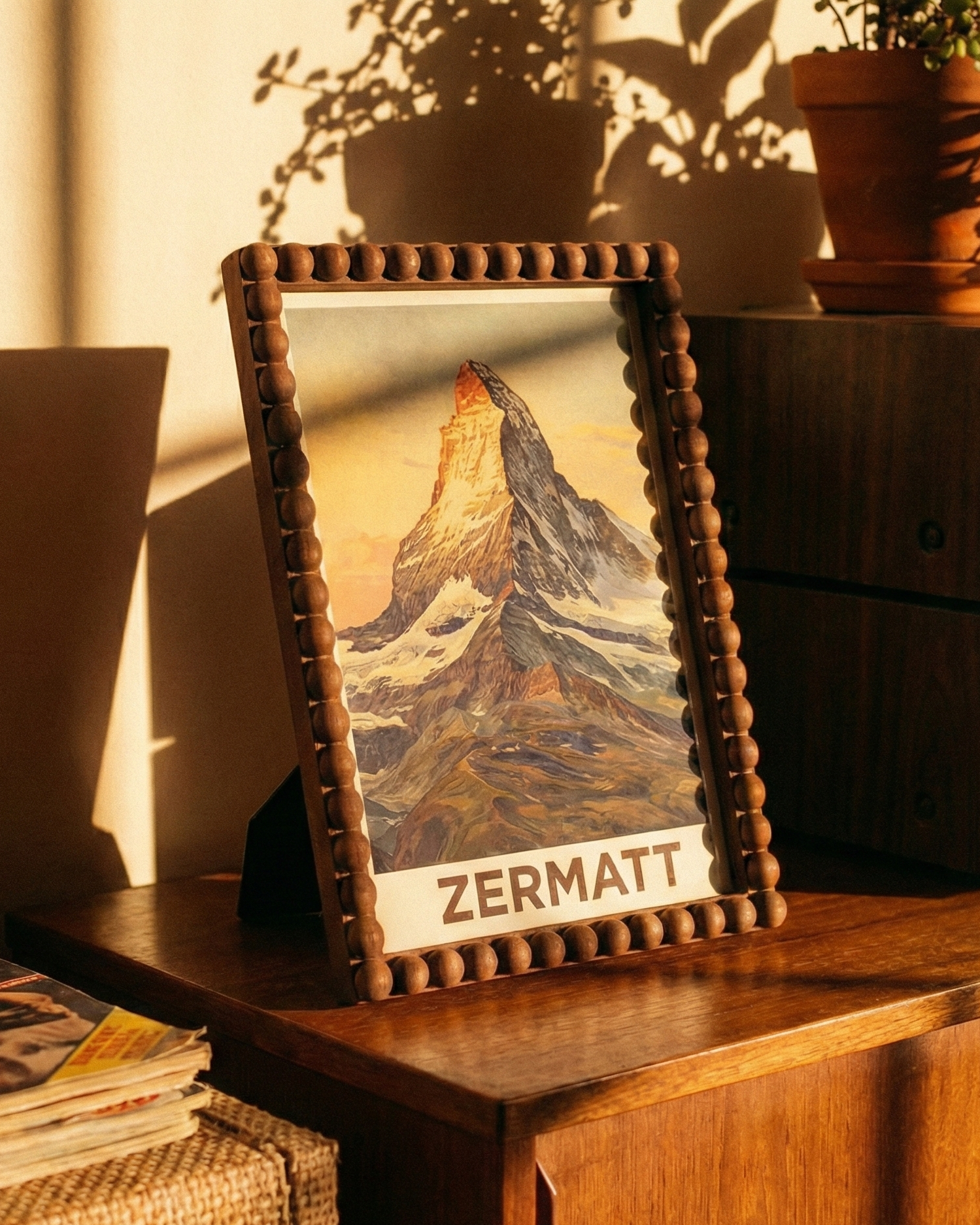 Framed picture of a mountain with 'Zermatt' text on a wooden surface with plants and a radio in the background.