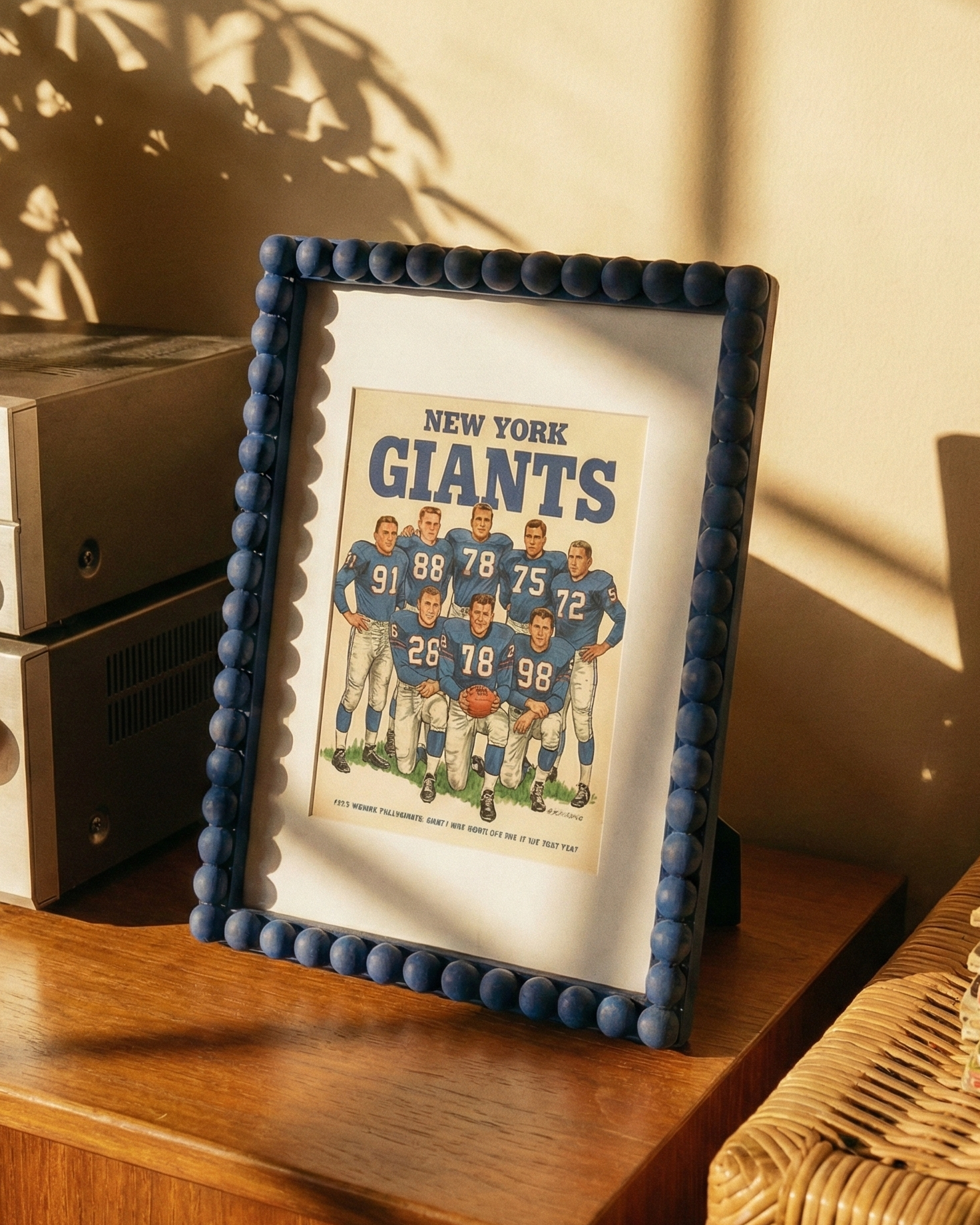 Framed New York Giants poster on a wooden surface with vintage stereo equipment and a plant in the background.