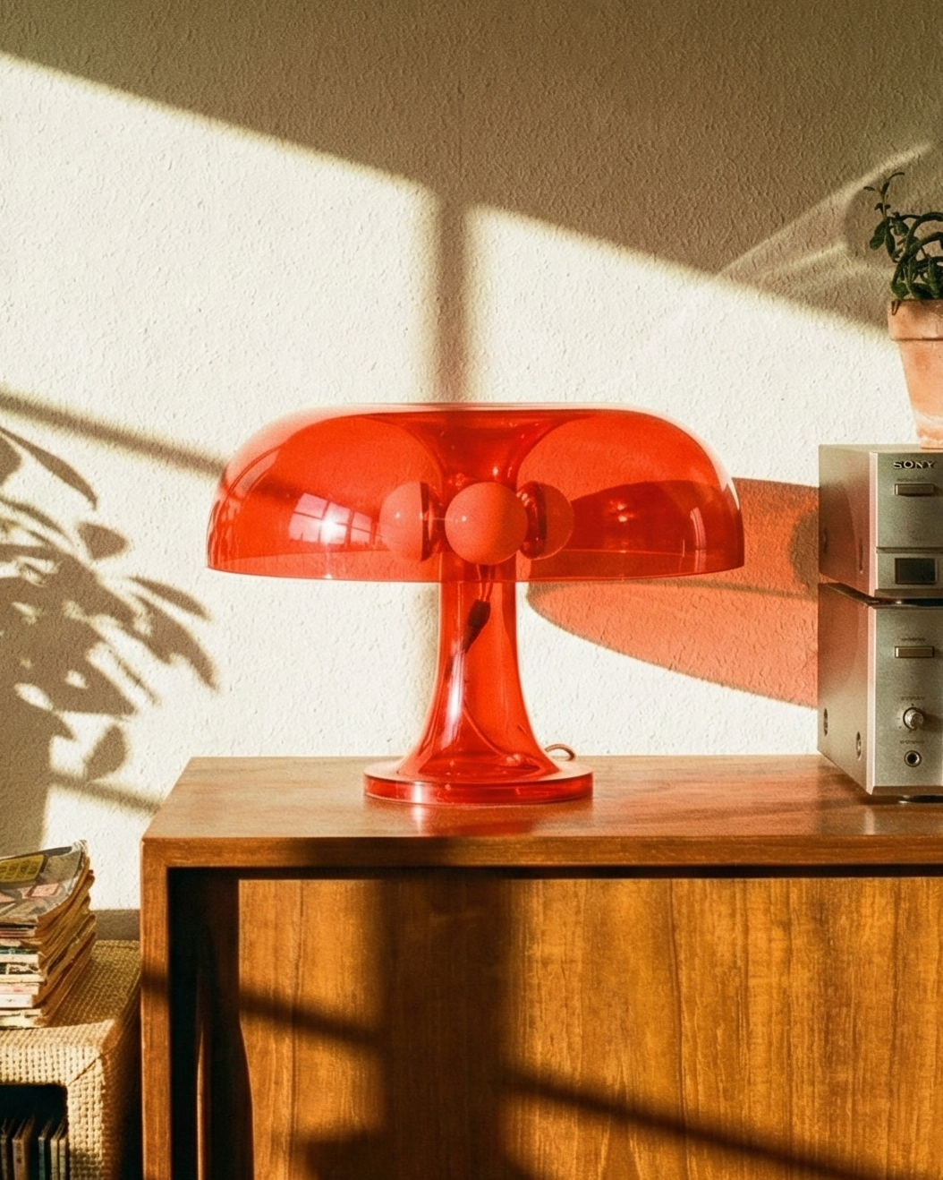 Wooden console table with a red lamp, vinyl records, and a vintage radio in a sunlit room.