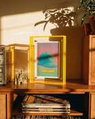 Wooden shelf with records, a framed picture, and a vintage radio in a warm-lit room.
