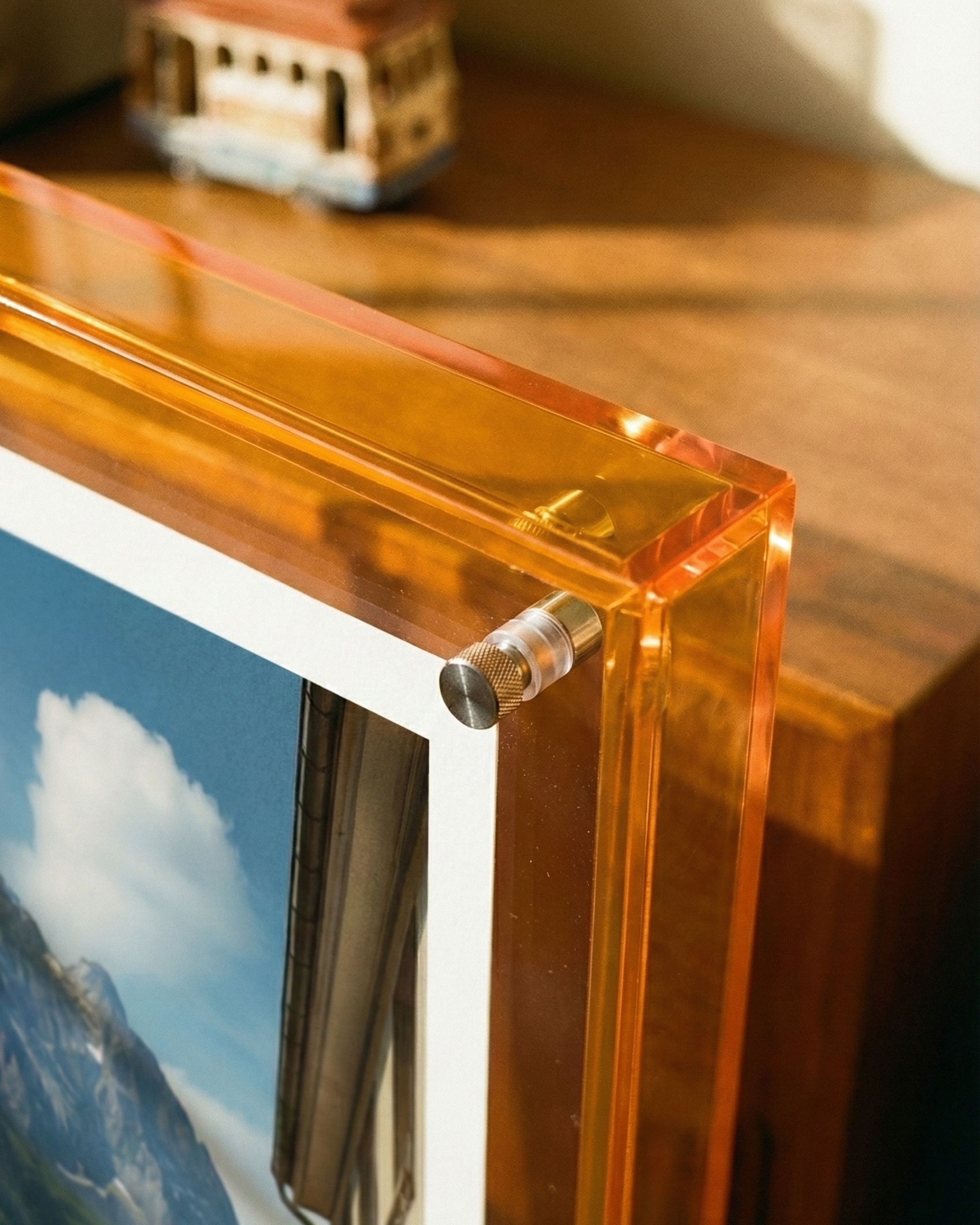Clear amber glass photo frame with a scenic print inside, placed on a wooden surface.
