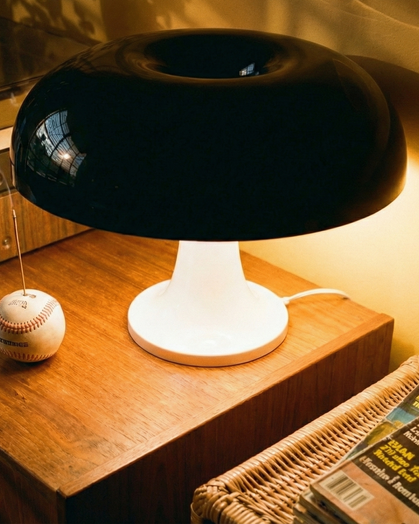 Black and white lamp on a wooden surface with a baseball and magazines in the background