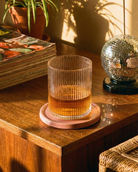 Glass of amber liquid on a wooden surface with a disco ball and books in the background
