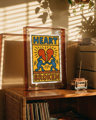 Framed artwork with 'Heart Broken' design on a wooden shelf with records and a vintage radio.