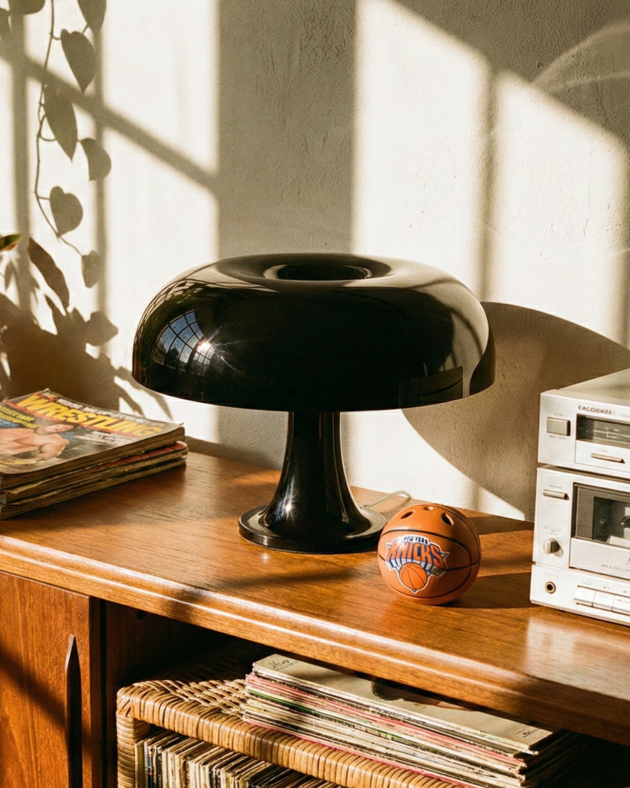 Wooden console table with vinyl records, a black lamp, and a vintage radio in a sunlit room.